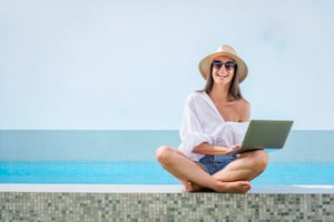 lachende Frau mit Laptop und Sonnenhut am Pool